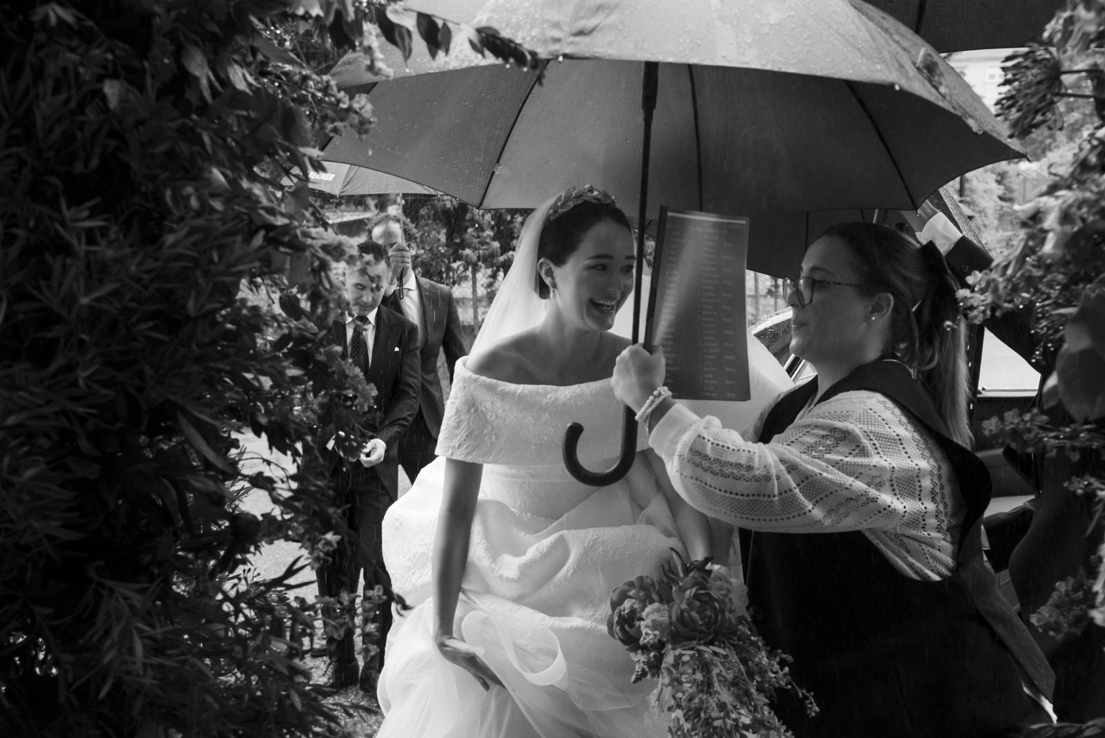 Wedding planner protegiendo a la novia de la lluvia con un paraguas